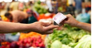 Manos intercambiando dinero en un mercado, representando cómo perder la pena de vender y ofrecer productos con confianza