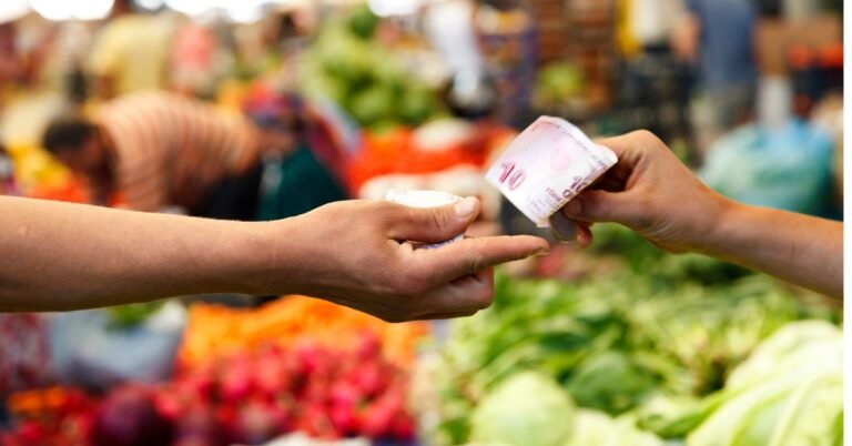 Manos intercambiando dinero en un mercado, representando cómo perder la pena de vender y ofrecer productos con confianza